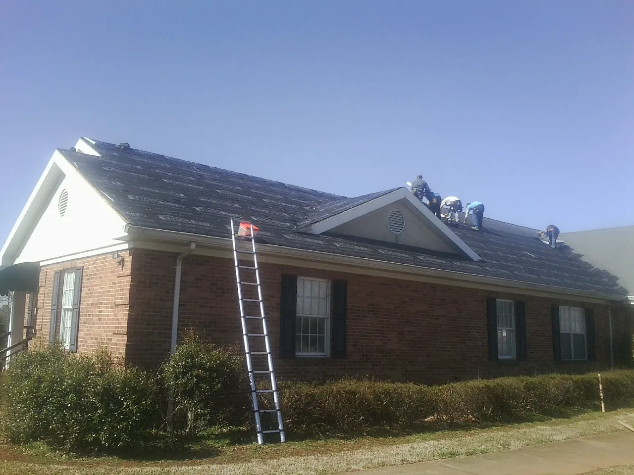 Crew tearing shingles off a brick ranch roof with a ladder set — Emergency Roof Repair work by our crew in Secaucus