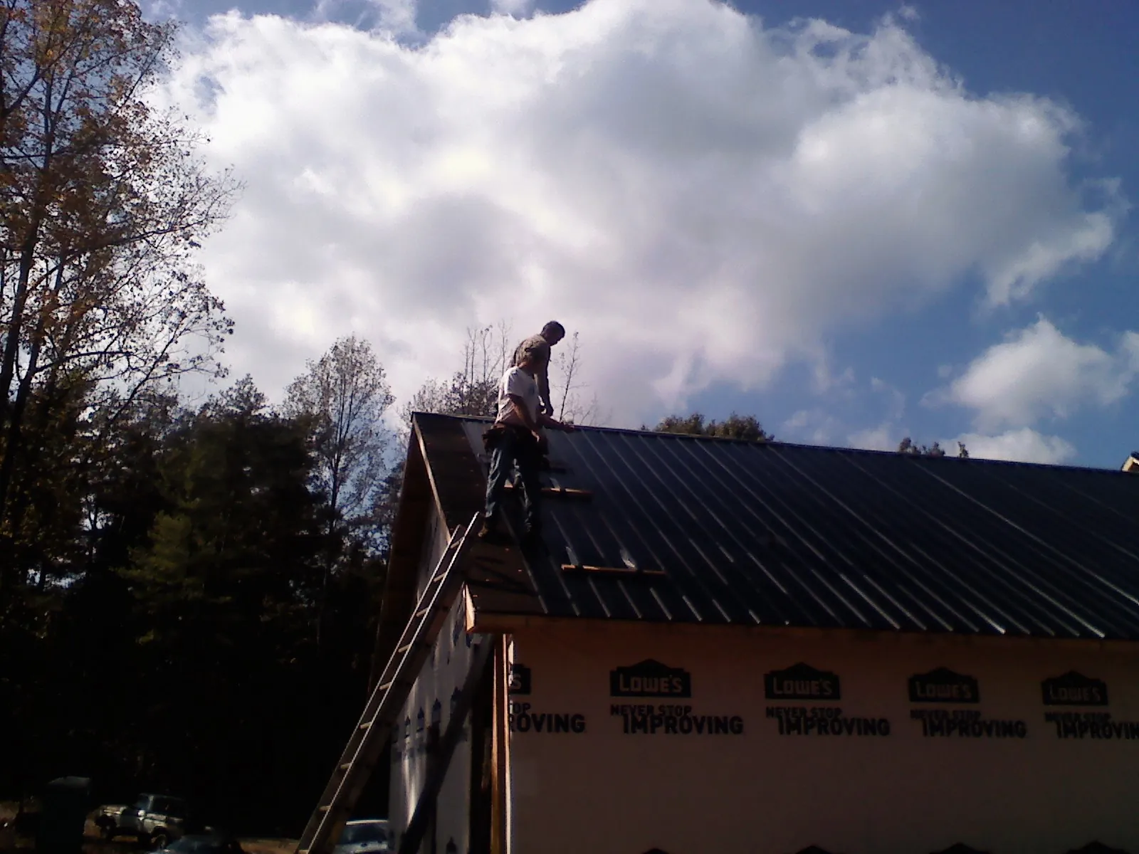 Roofer fastening dark metal panels high against a cloudy sky, from a Roof Inspection job in Secaucus
