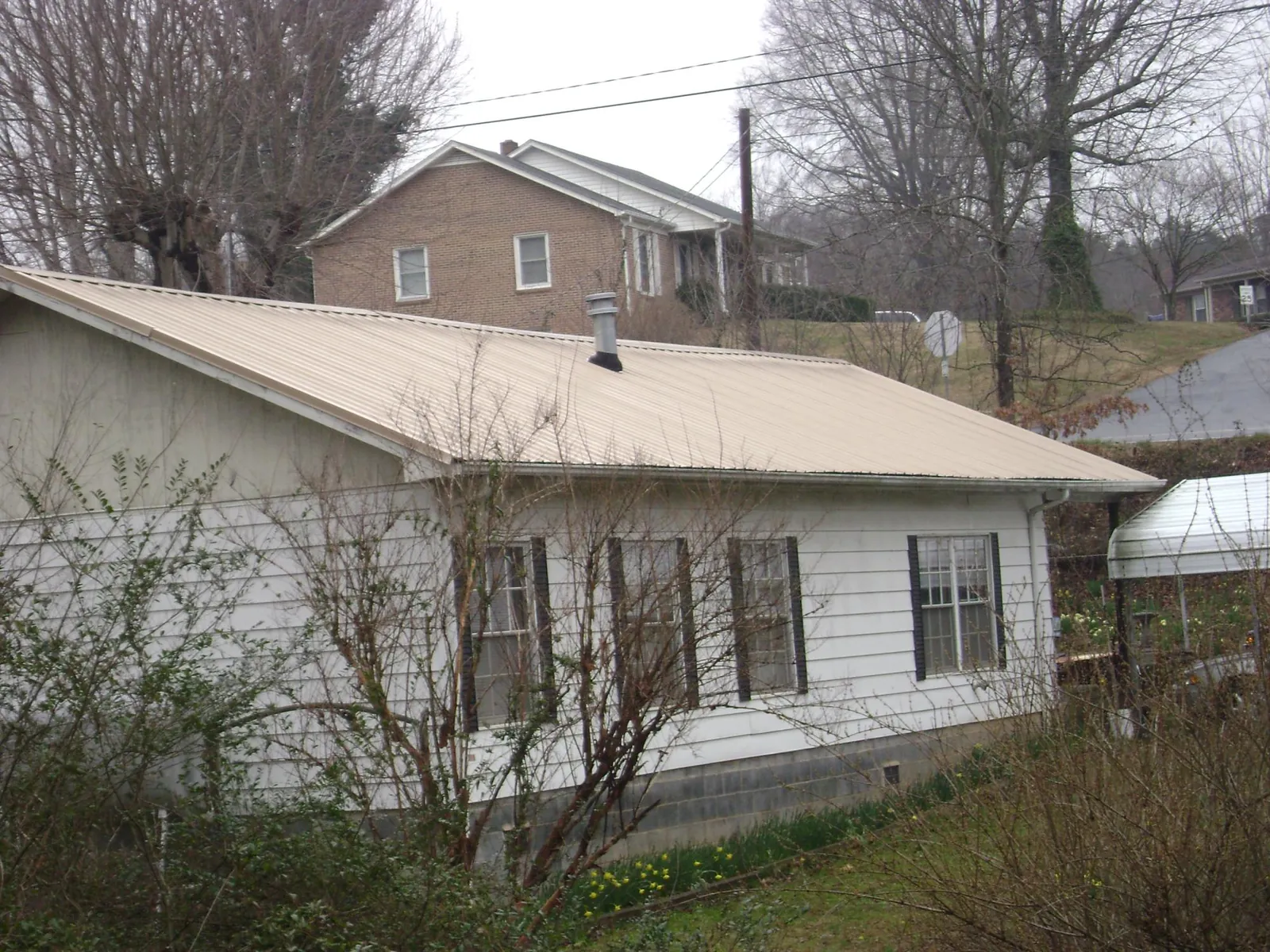 Tan metal roof on a white sided house set into a hillside — Commercial Roofing by Roofing Brothers in Secaucus